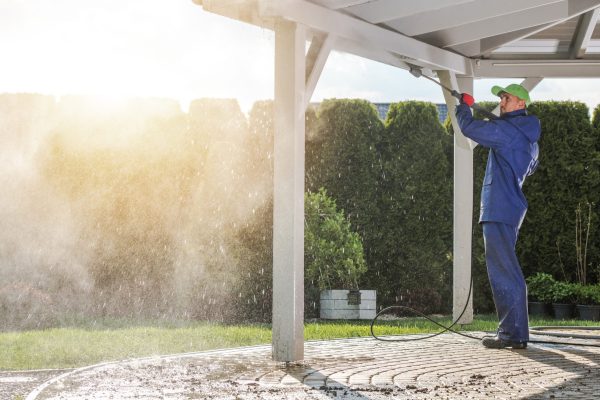 A Caucasian Worker with a pressure washer cleaning the roof of a Patio House